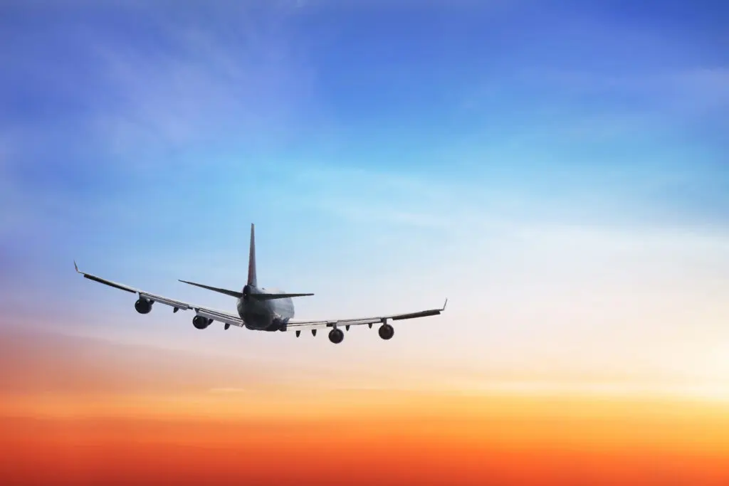 Commercial plane flying through sunset with orange and blue skies
